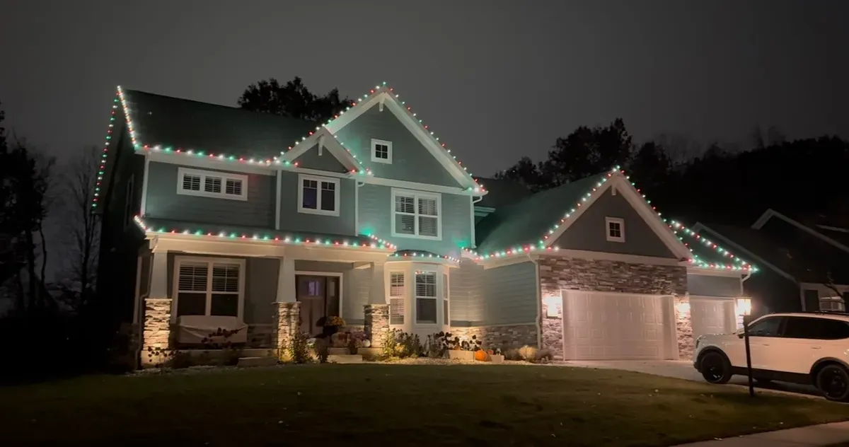 A two-story home with red, green and white lights along the rooflines and gables