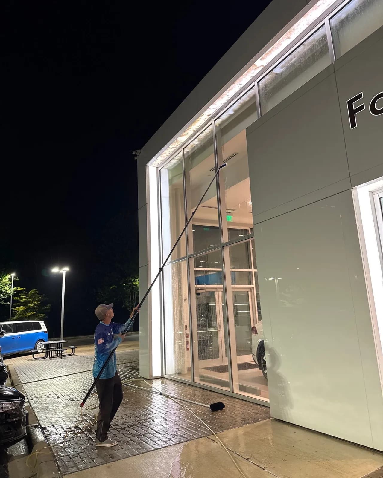 Cleaning a dealership's glass storefront at night with a pole