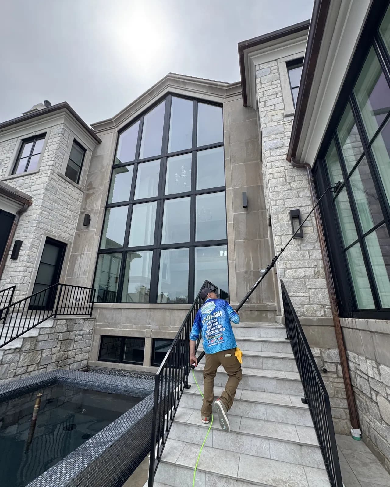 Andrew cleaning the tall windows of a stone home with a pole